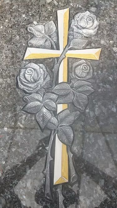 Gelb-weißes Kreuz mit grauen Rosen, eingraviert in eine Steinoberfläche