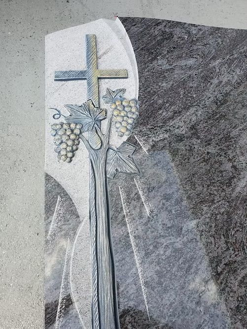 Ein Kreuz mit Trauben und Weizen, eingraviert in eine Gedenktafel aus grauem Stein.