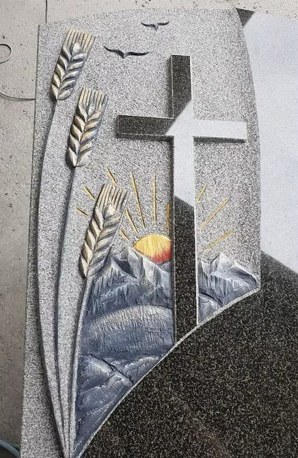 Religiöse Grabsteingravur mit einem Kreuz, Weizenähren und einem Sonnenaufgang über Bergen in Grau und Gold.