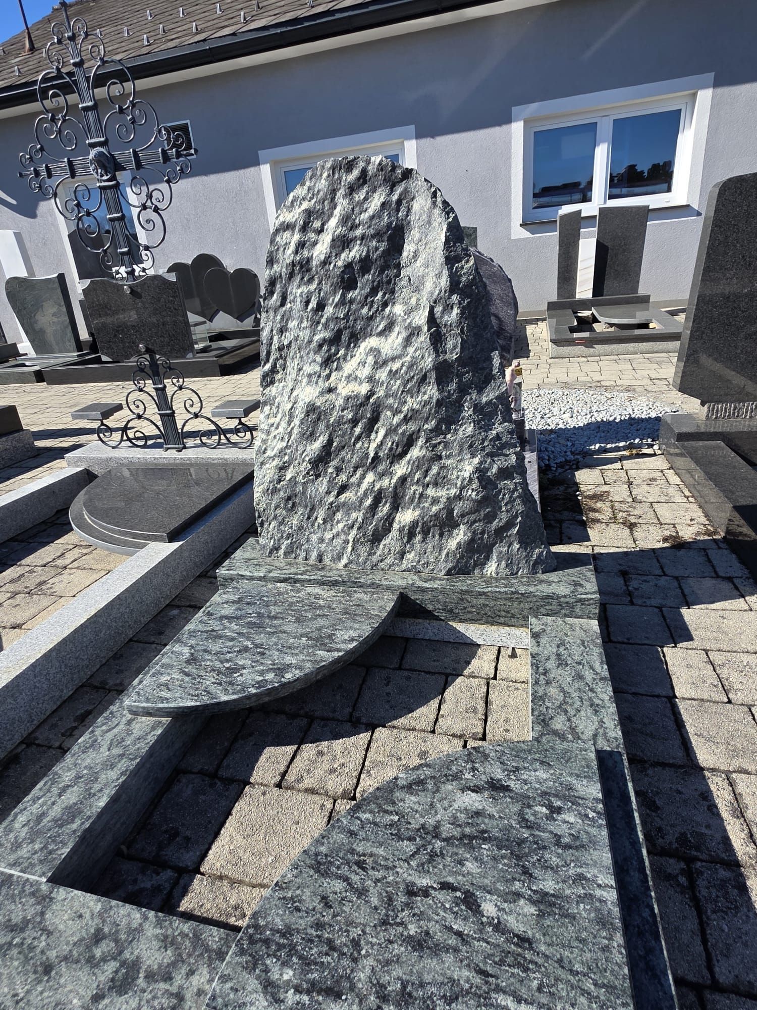 Graues Steinmonument mit passenden Steinplatten in einem sonnigen Innenhof vor einem Haus