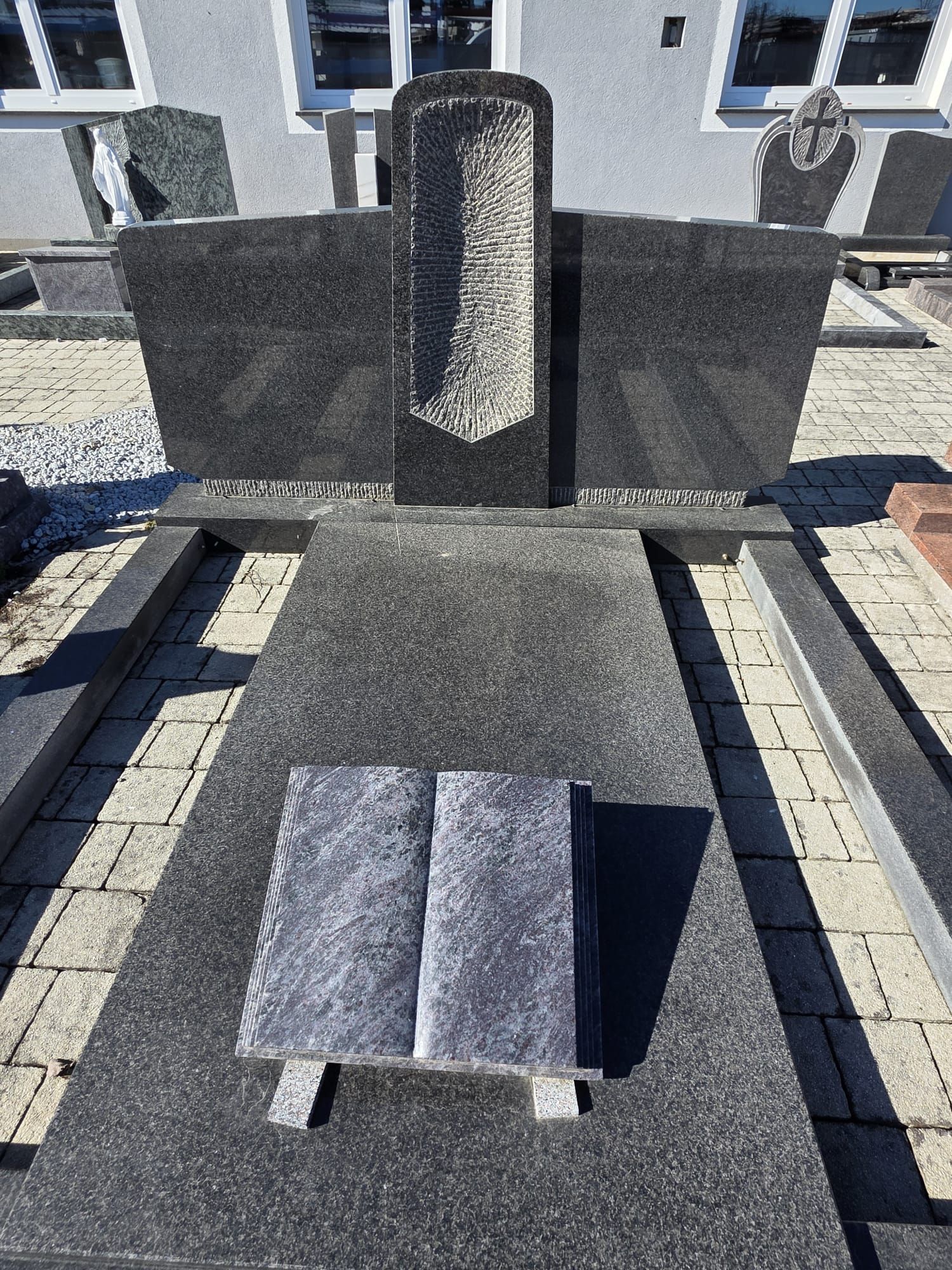 Gedenkstätte im Freien mit einem Granitgrabstein und zwei flachen Steinbänken auf einer gepflasterten Fläche