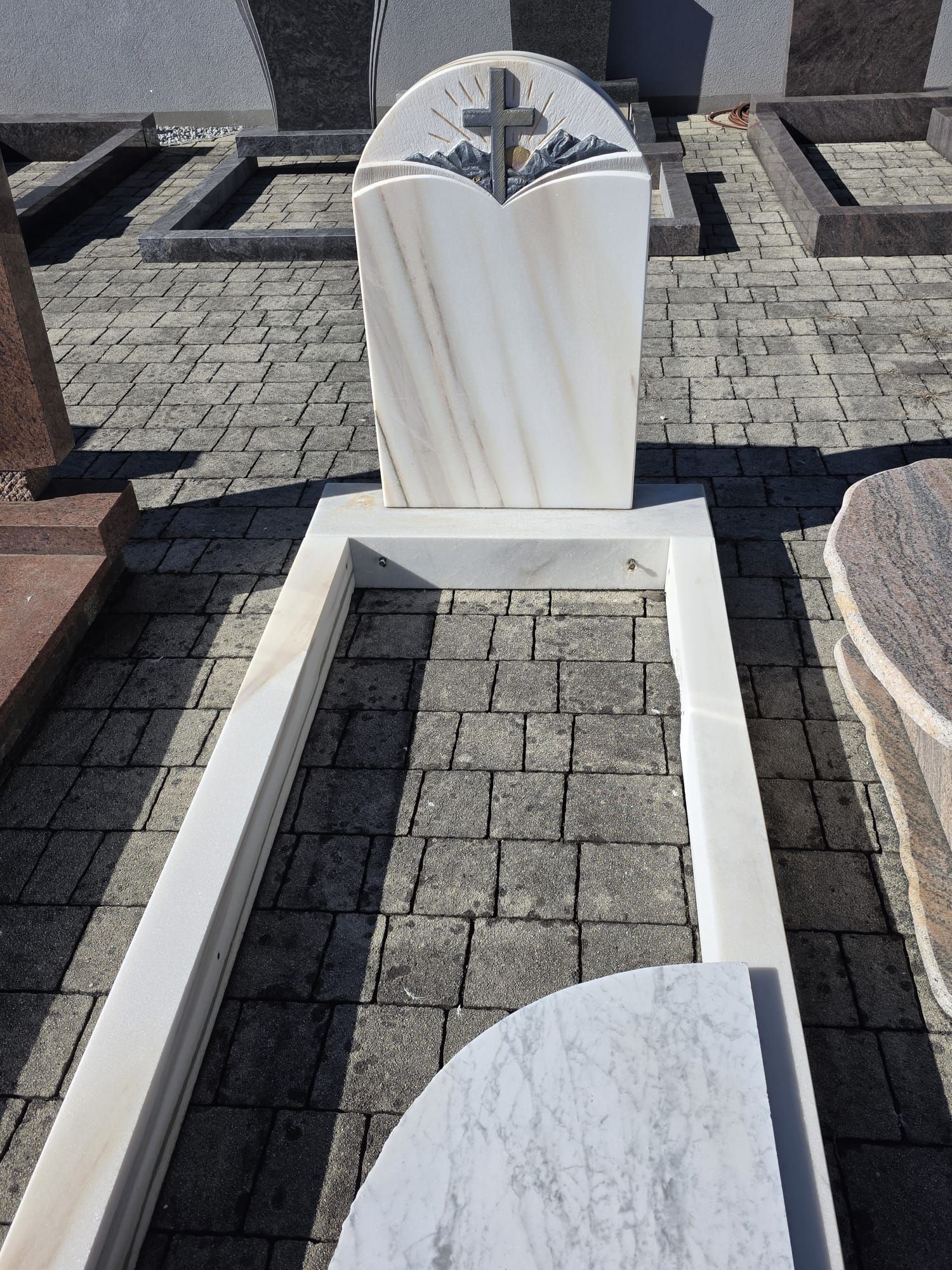 Grabmal aus weißem Marmor mit Kreuz, aufgestellt auf einem gefliesten Friedhofsplatz