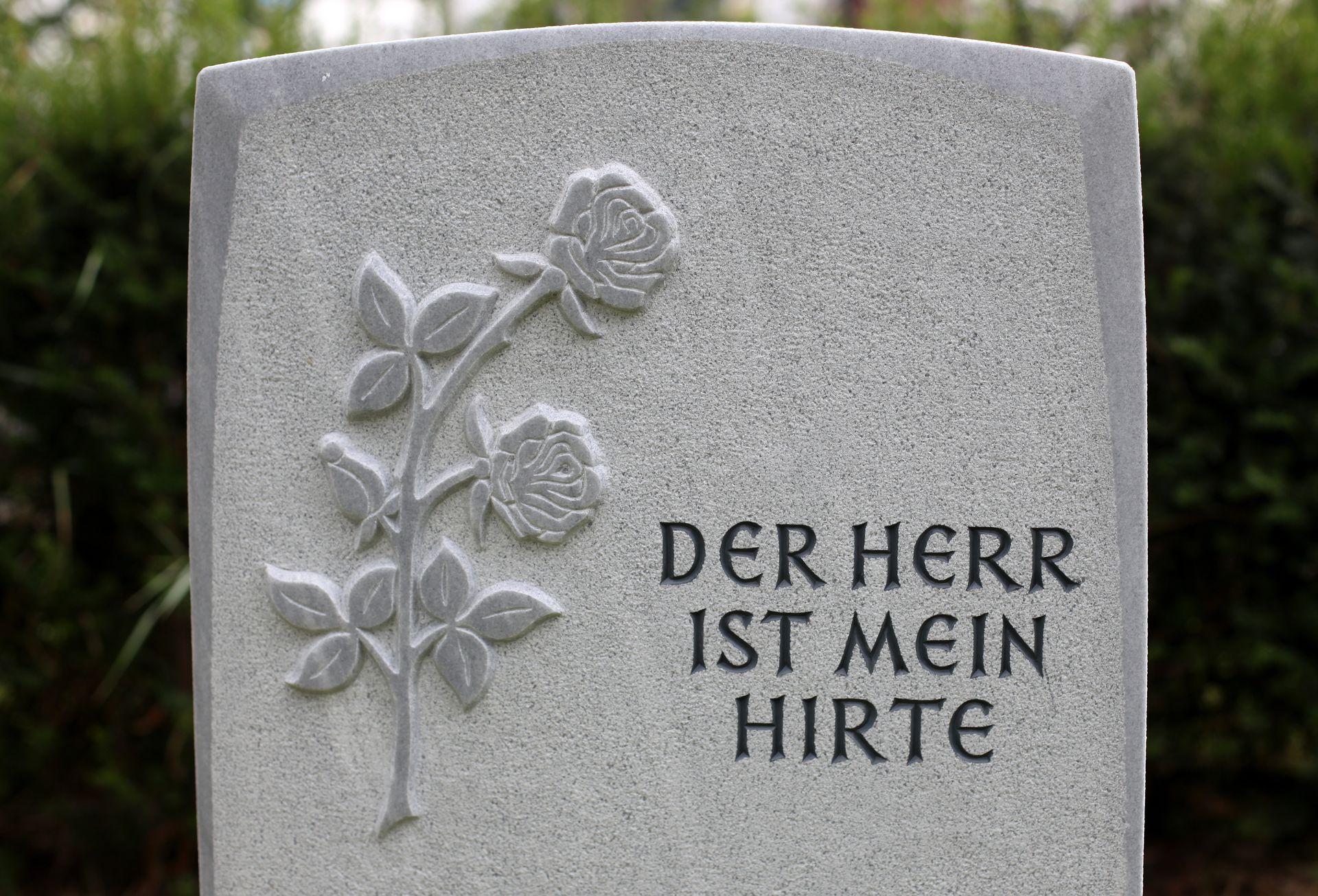 Gray gravestone with carved flowers and the German inscription “DER HERR IST MEIN HIRTE”