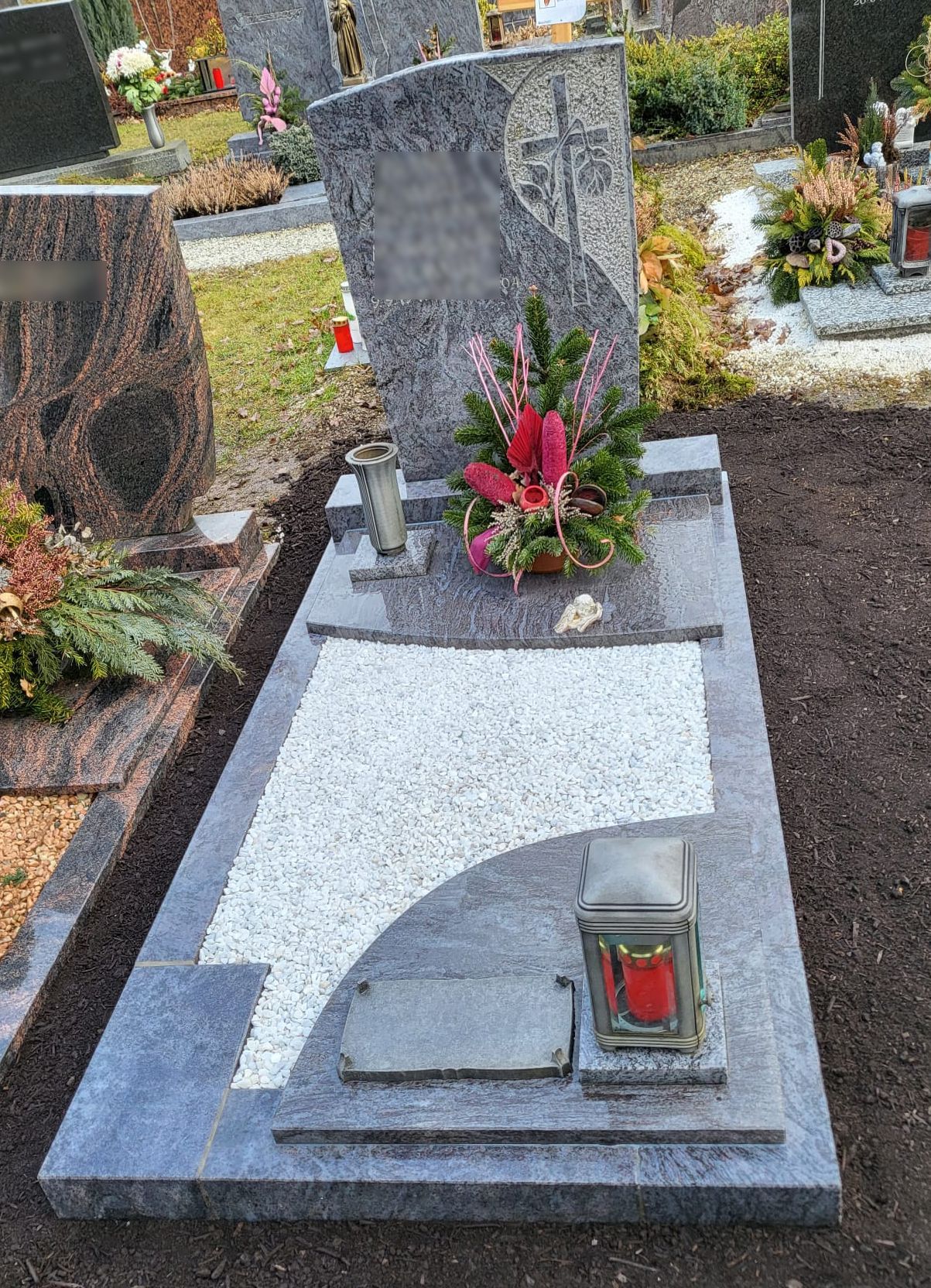 Grau-weißer Grabstein mit roten Blumen und einer Laterne auf einem Friedhof