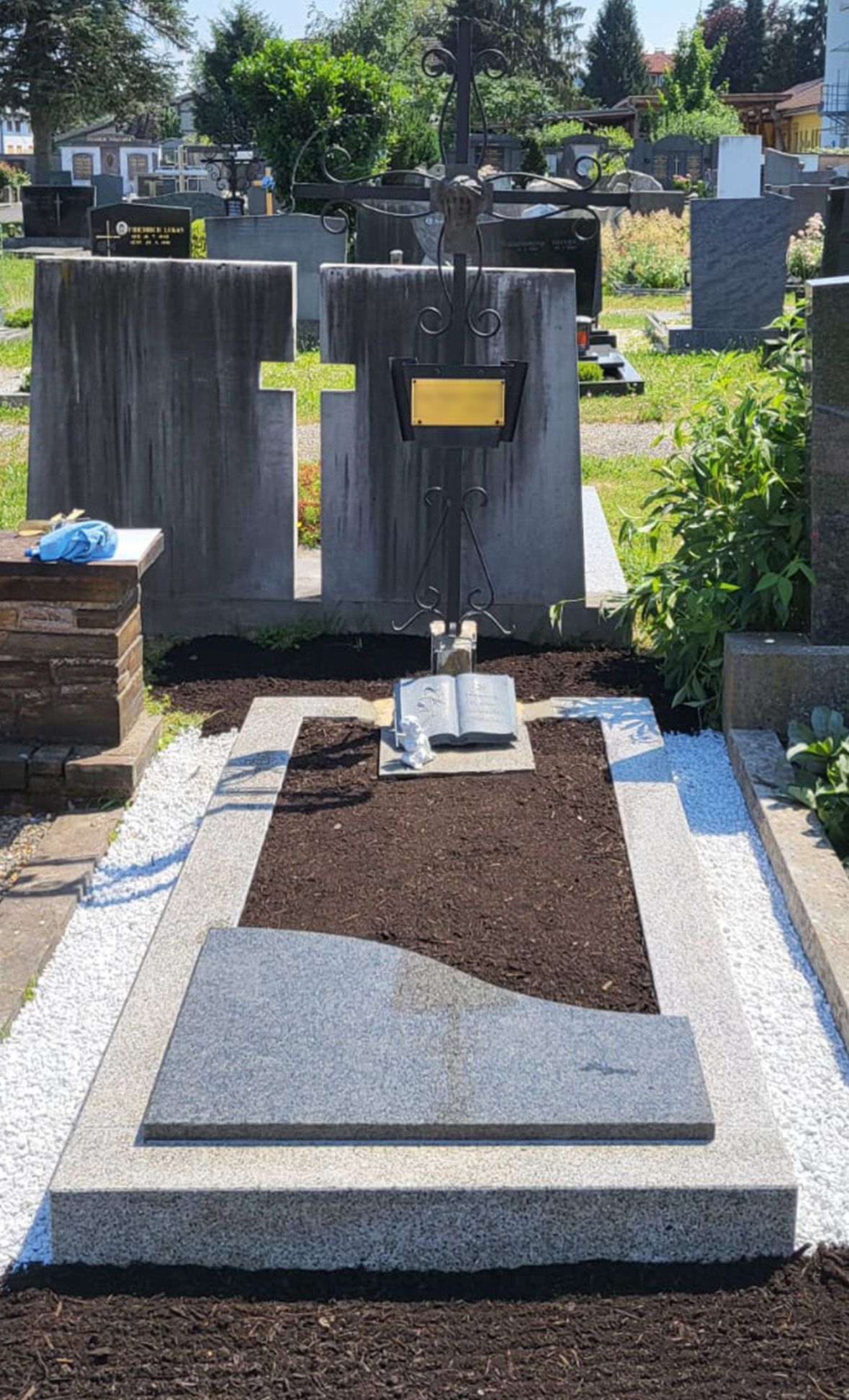 Grabstein mit schwarzem Grabstein, gelben Kreuzen und frischer Erde auf einem Friedhof