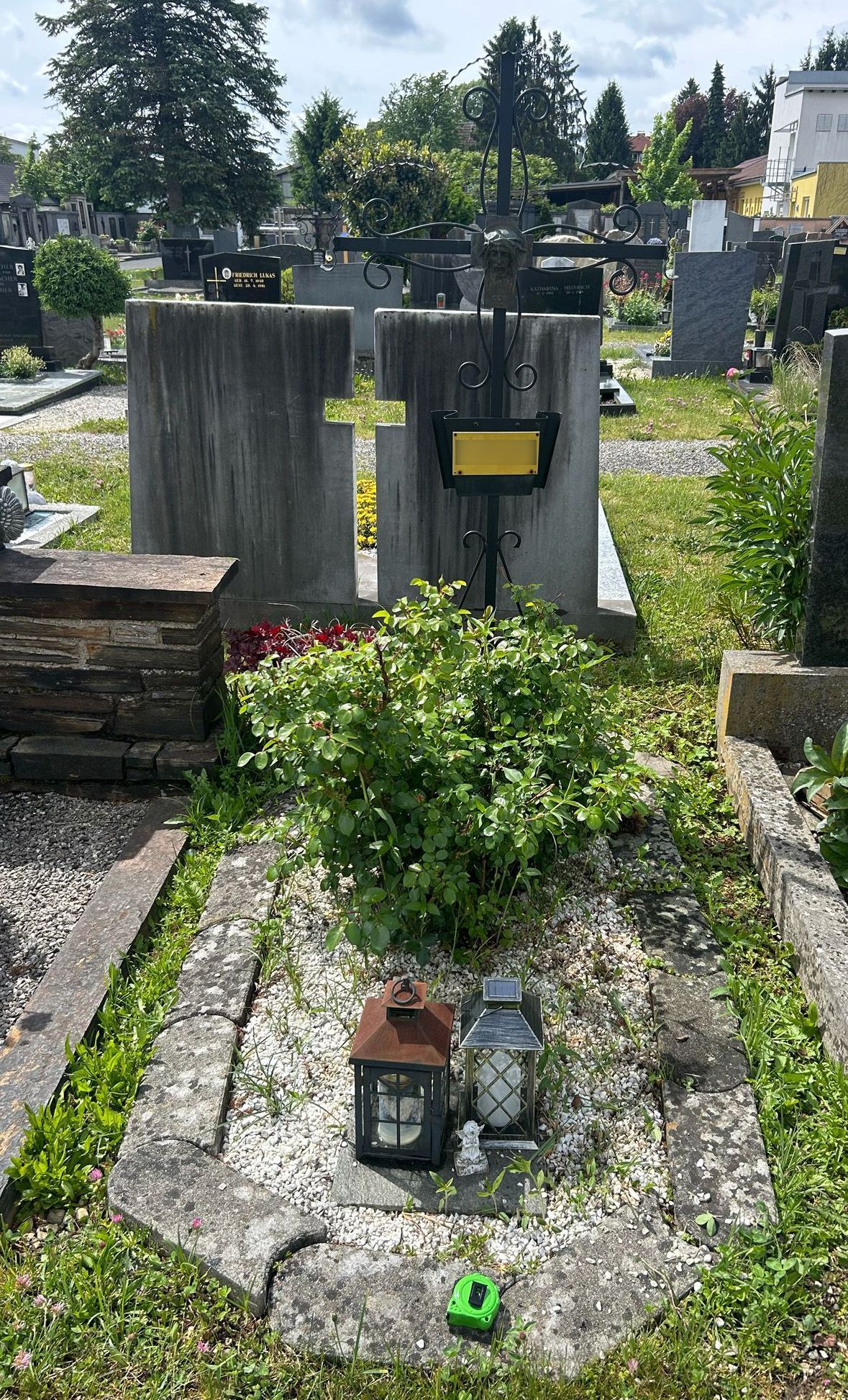 Gräber auf einem Friedhof, mit kleinen Gedenksteinen, Blumen und Grabsteinen unter Bäumen.