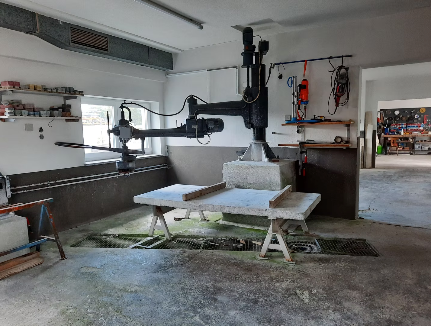 Große Steinschneidemaschine in einer Werkstatt, mit Arbeitstisch und Werkzeugen vor weißen Wänden.