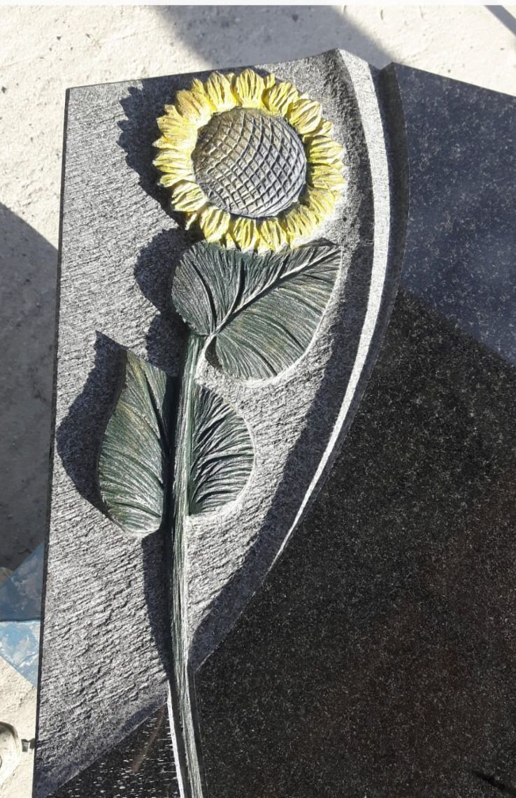 Sonnenblumenrelief mit gelben Blütenblättern und grünen Blättern auf einer dunklen Steinplatte