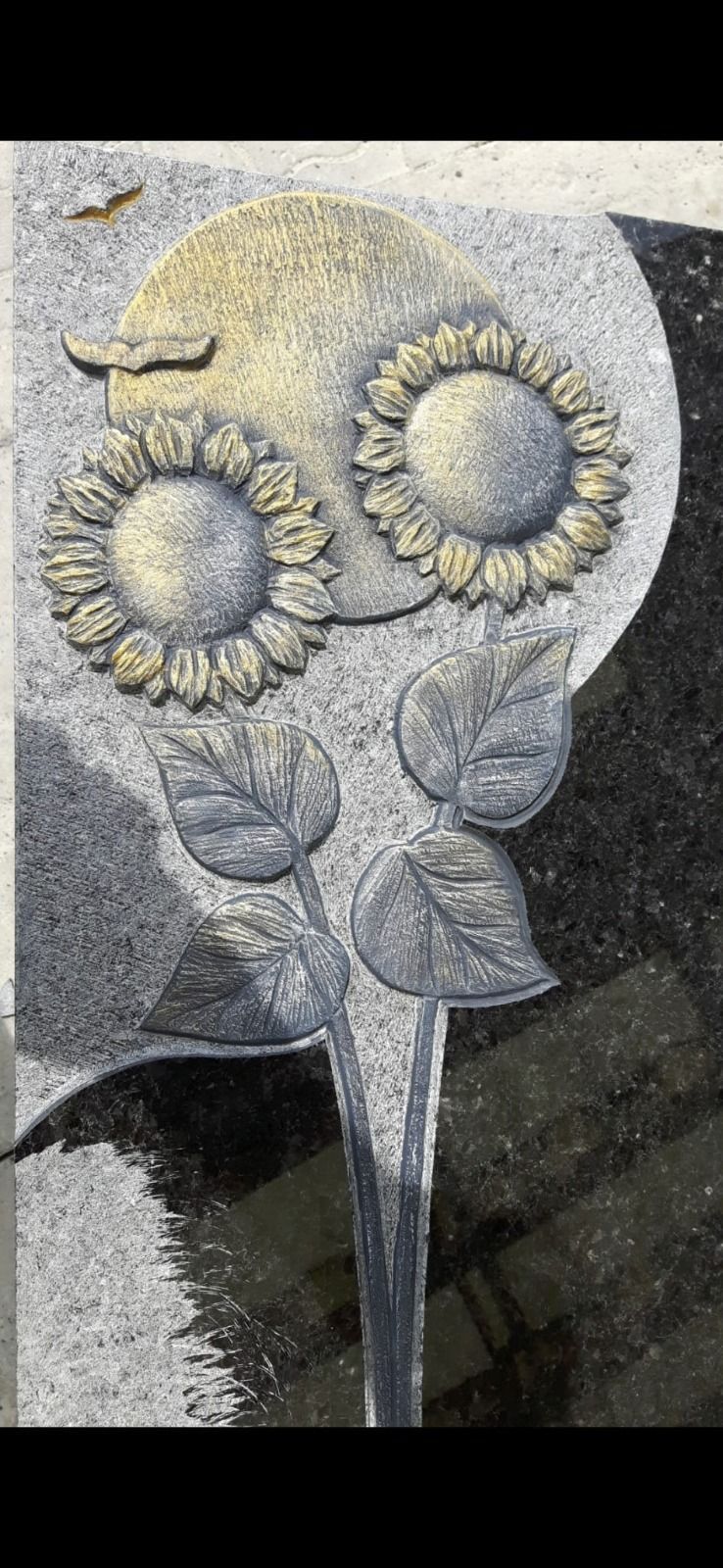 Graue Steinskulptur einer Sonnenblume mit zwei runden Blüten und Blättern auf dunklem Hintergrund