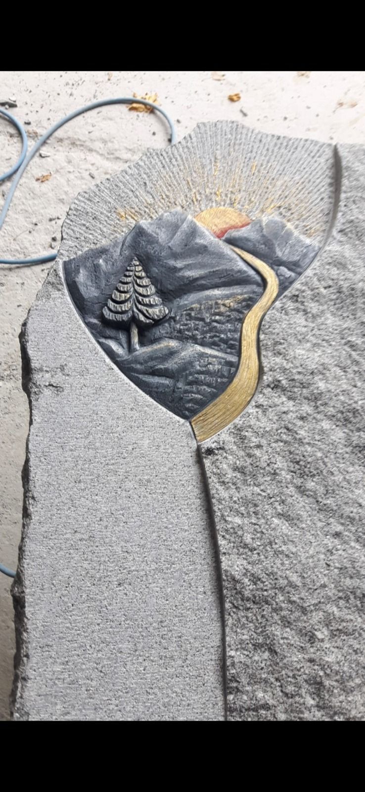 Grabtsein mit gesprenkelter Oberfläche mit goldenem, geschwungenem Rand und einem Baummotiv in der Mitte.