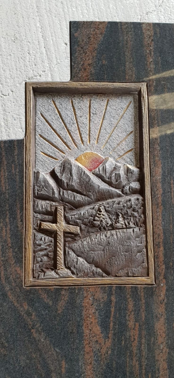 Holzrelief eines Sonnenaufgangs über Bergen mit einem Kreuz im Vordergrund