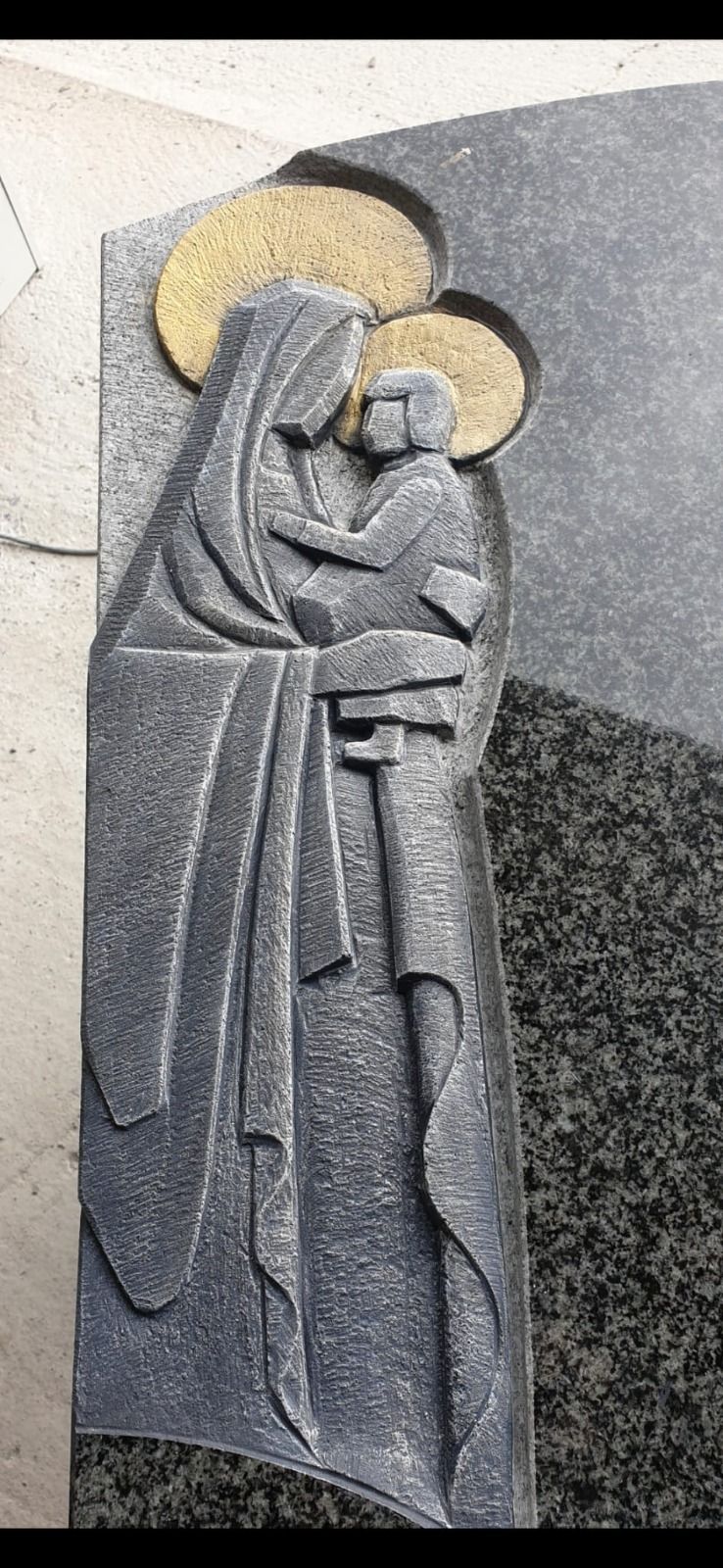 Steinrelief einer in ein Gewand gehüllten Figur, die ein Kind im Arm hält, mit goldenen Heiligenscheinen