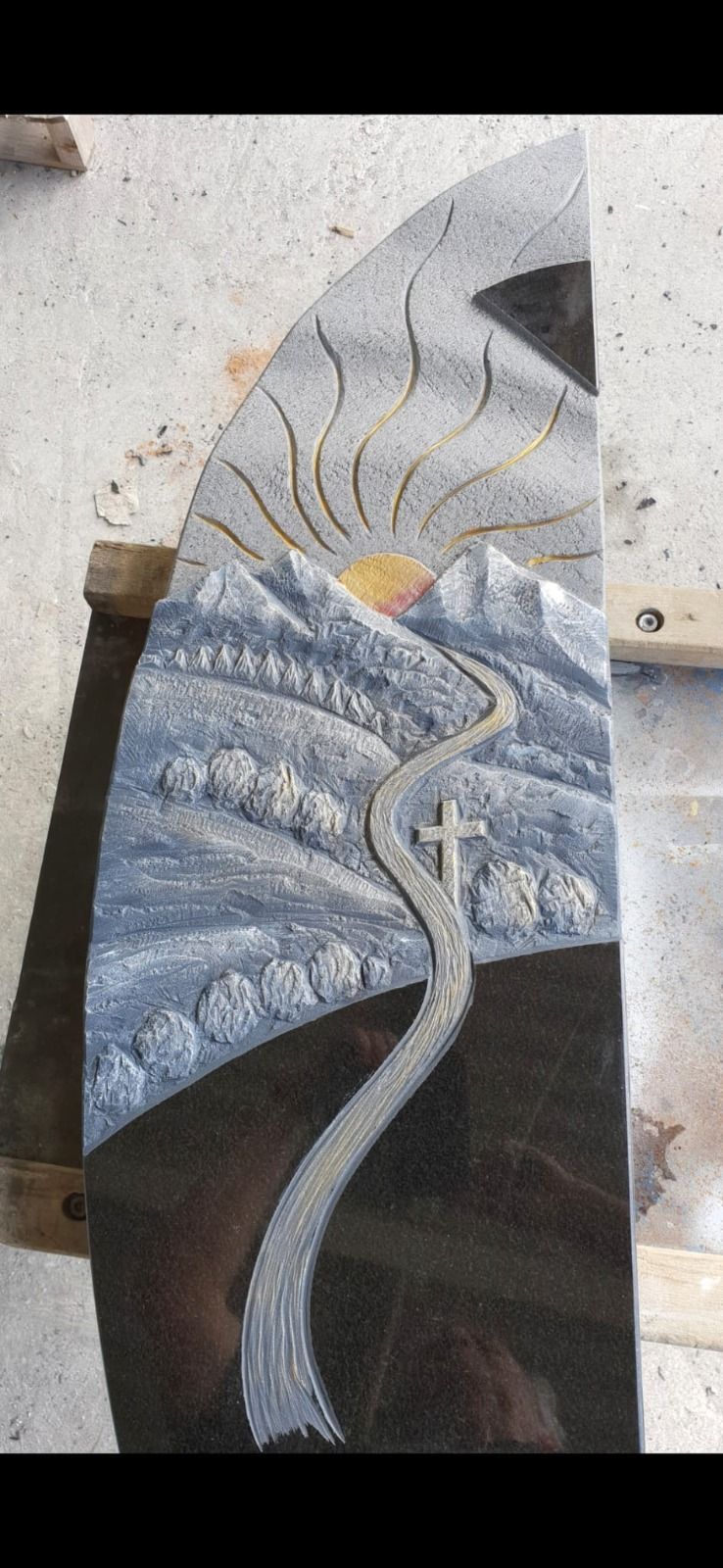 Abstrakt bemalter Stein mit einem Baum, geschichteten blauen Hügeln und einem schwarzen Himmel mit einem gelben Sonnenstrahl.