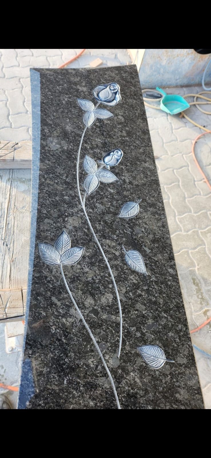 Schwarze, polierte Steinplatte mit eingraviertem weißen floralen Rankenmuster und Blättern auf einem Ziegelboden