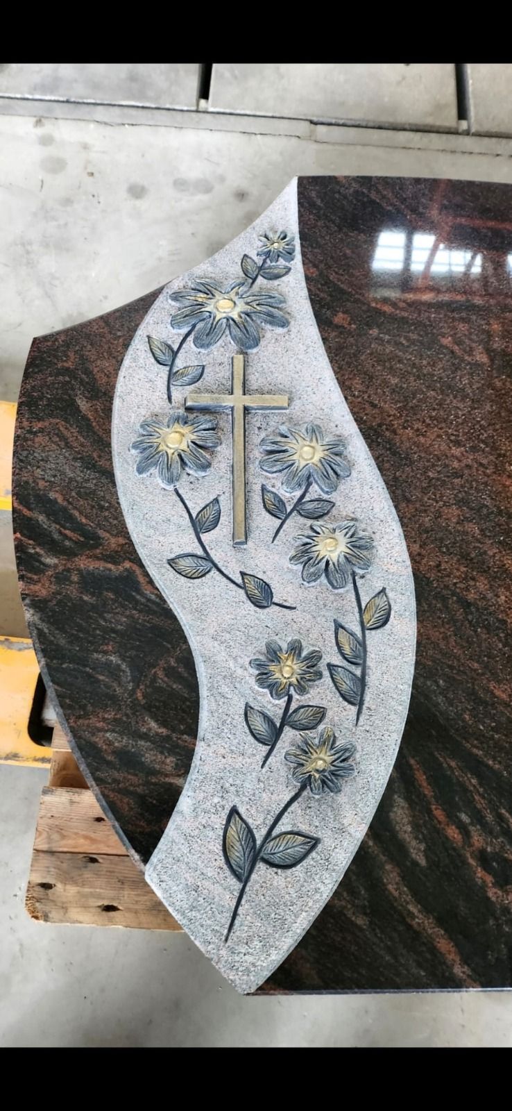 Dekorative Steinplatte mit einem hellen floralen Kreuzmuster auf dunklem, strukturiertem Hintergrund