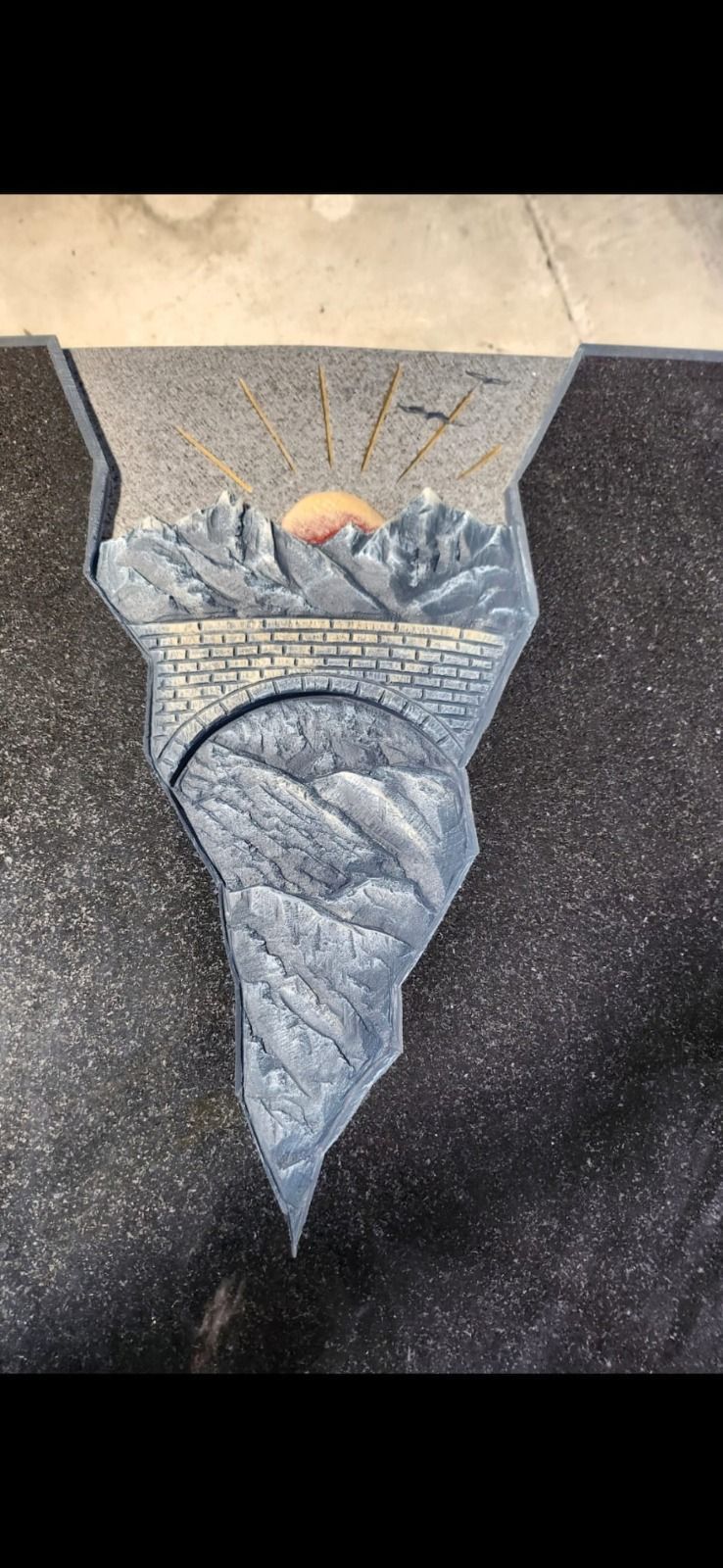 Ein aus Stein gehauenes Relief einer Glocke, die über einer spitz zulaufenden Ziersäule in einer Wandnische hängt.