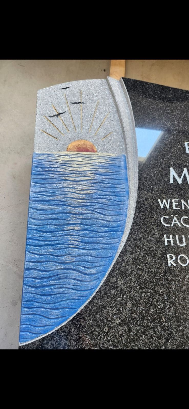 Abstraktes Mosaik einer aufgehenden Sonne über blauem Wasser neben einem schwarzen Schild mit weißer Schrift
