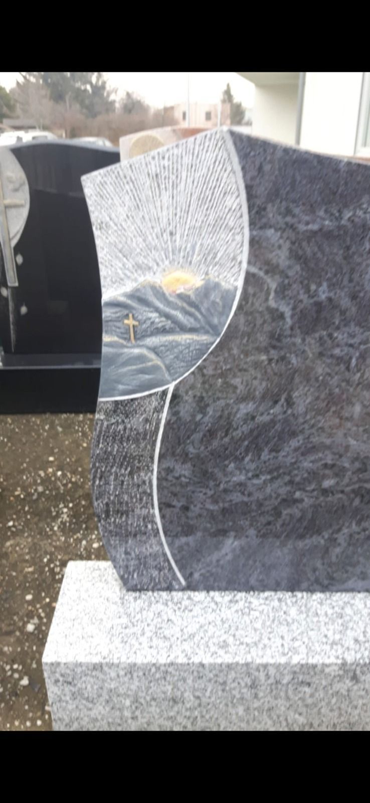 Grabstein mit einer runden, polierten Plakette und strukturiertem grauen Stein auf einem Friedhof