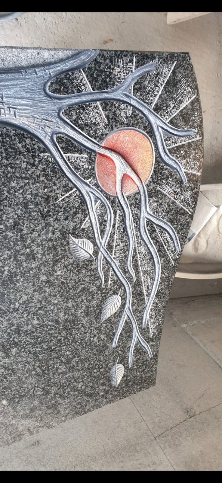 Grabstein mit verzweigten weißen Linien und einem rosa-orangenen Kreis auf dunklem Untergrund