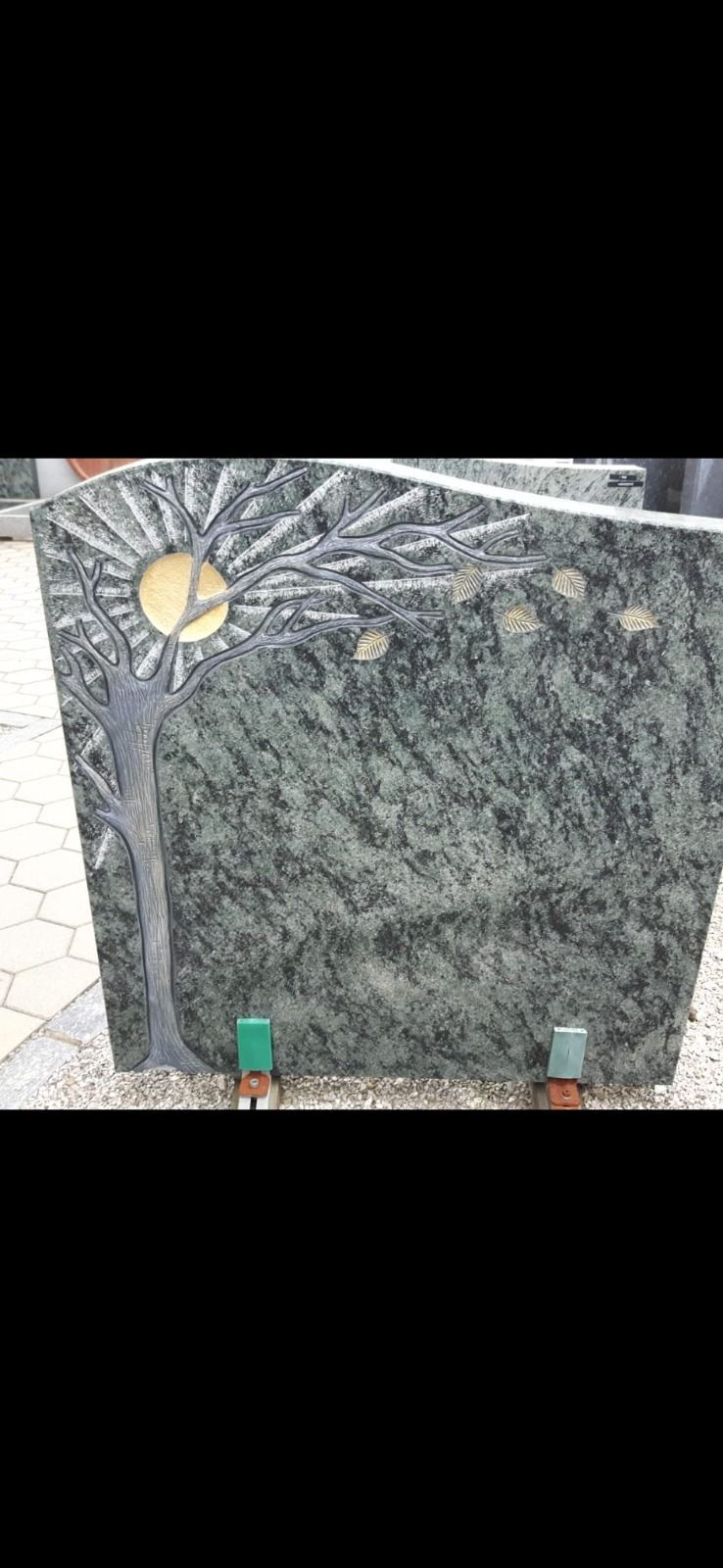 Polierte, dunkle Steingedenktafel mit kleinem Sonnenmotiv und zwei Stützen am Sockel