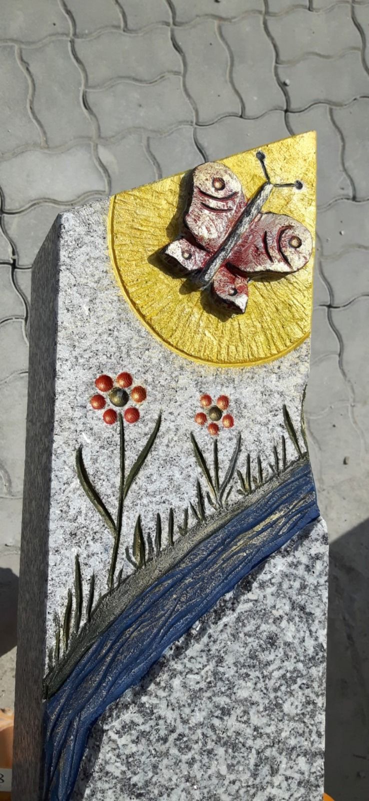 Farbenfrohes Mosaik aus einem Schmetterling über Blumen und einem blauen Bach auf einer strukturierten Wand