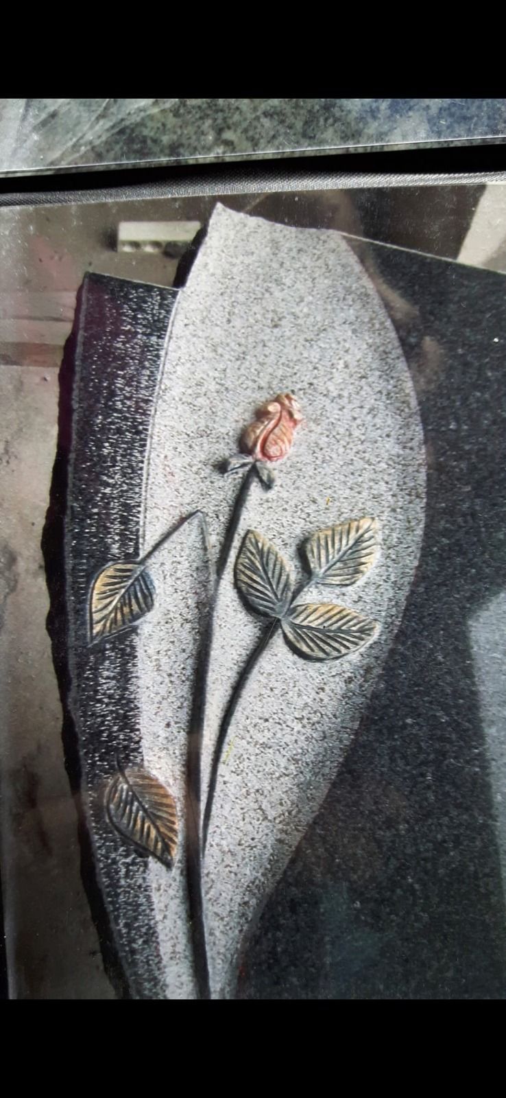 Ein dekoratives Blumenmuster auf einer grauen, blattförmigen Plakette mit einer rosa Blüte und goldenen Blättern.