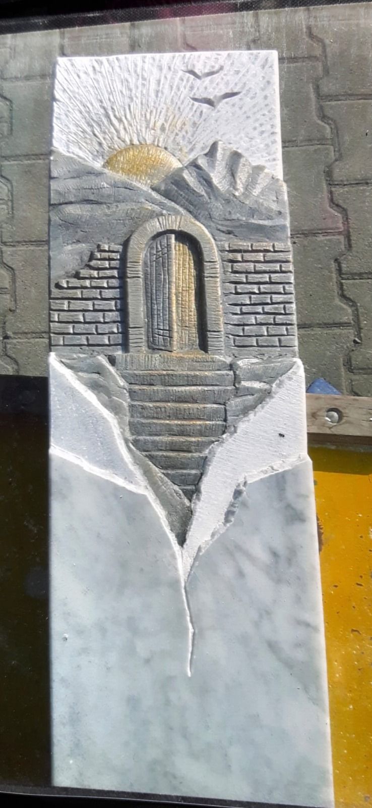 Steinrelief einer Sonne über einem Bogenportal, eingerahmt von weißen Flügeln an einer grauen Wand