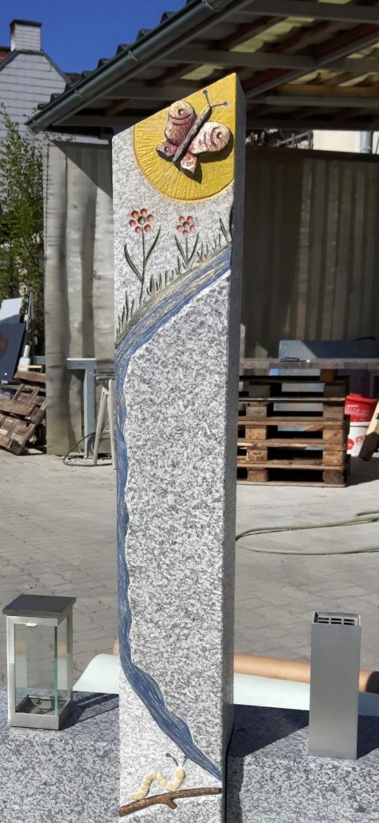 Hohe Mosaiksteinsäule mit einem gelben Schmetterlingsmosaik an der Spitze in einem Außenhof.