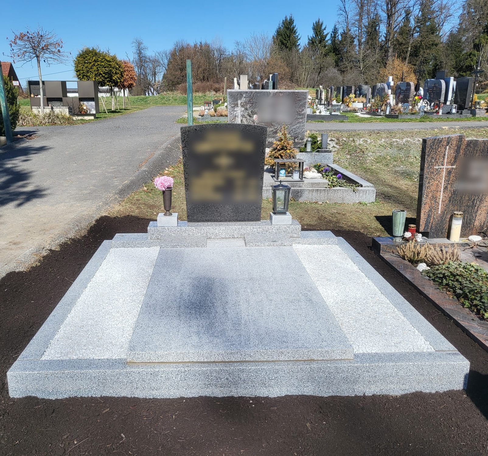 Ein Grabdenkmal auf einem Friedhof mit grauem Steinsockel und verschwommenem Grabstein unter klarem Himmel
