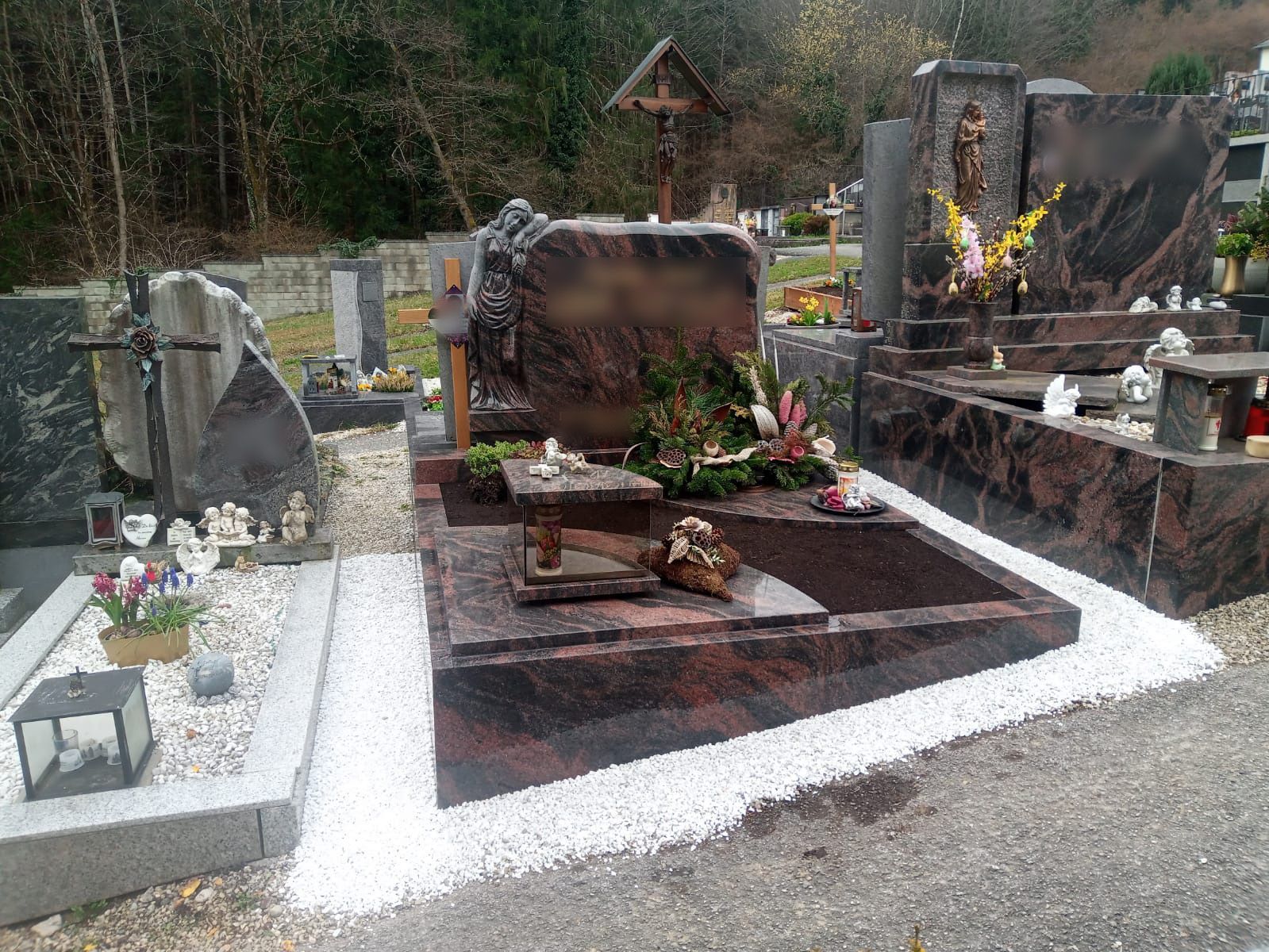Ein mit Blumen geschmücktes Grab und ein Denkmal aus rotem Stein auf einem Friedhof, der von weißem Kies umgeben ist.