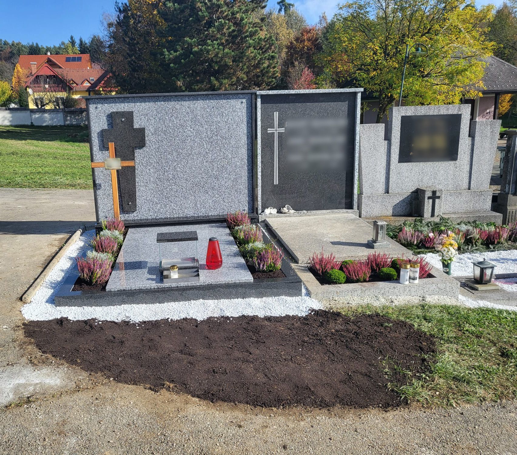 Gedenkgrab mit Kreuzen, Blumen und Steintafeln auf einem Friedhof unter sonnigem Himmel