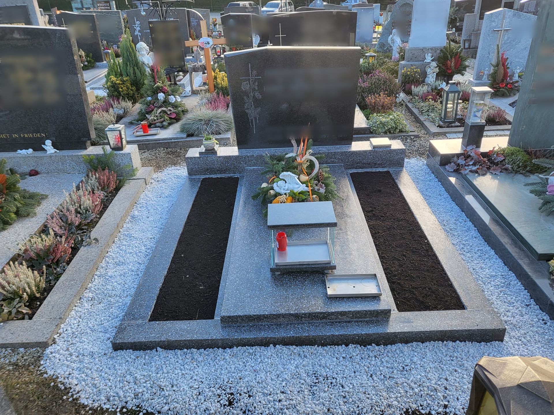 Modernes Friedhofsgrab mit schwarz-weißer Steinumrandung, Blumen und einem großen Grabstein.