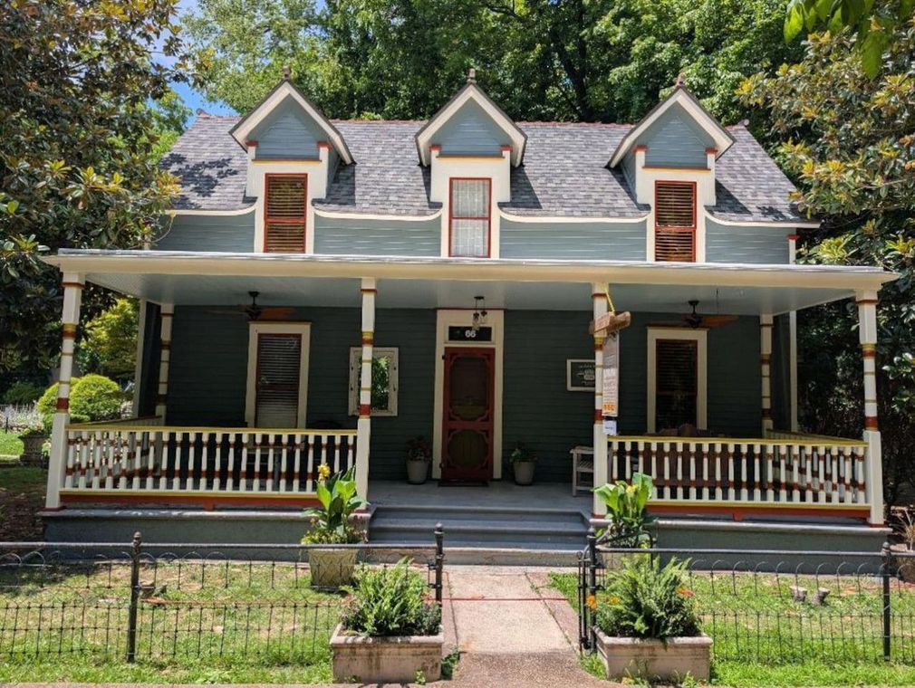 Victorian-style house with green porch, white trim, and dormer windows behind a front garden