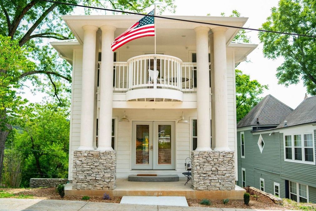 Front view of a white-columned house with a balcony and an American flag by the entrance