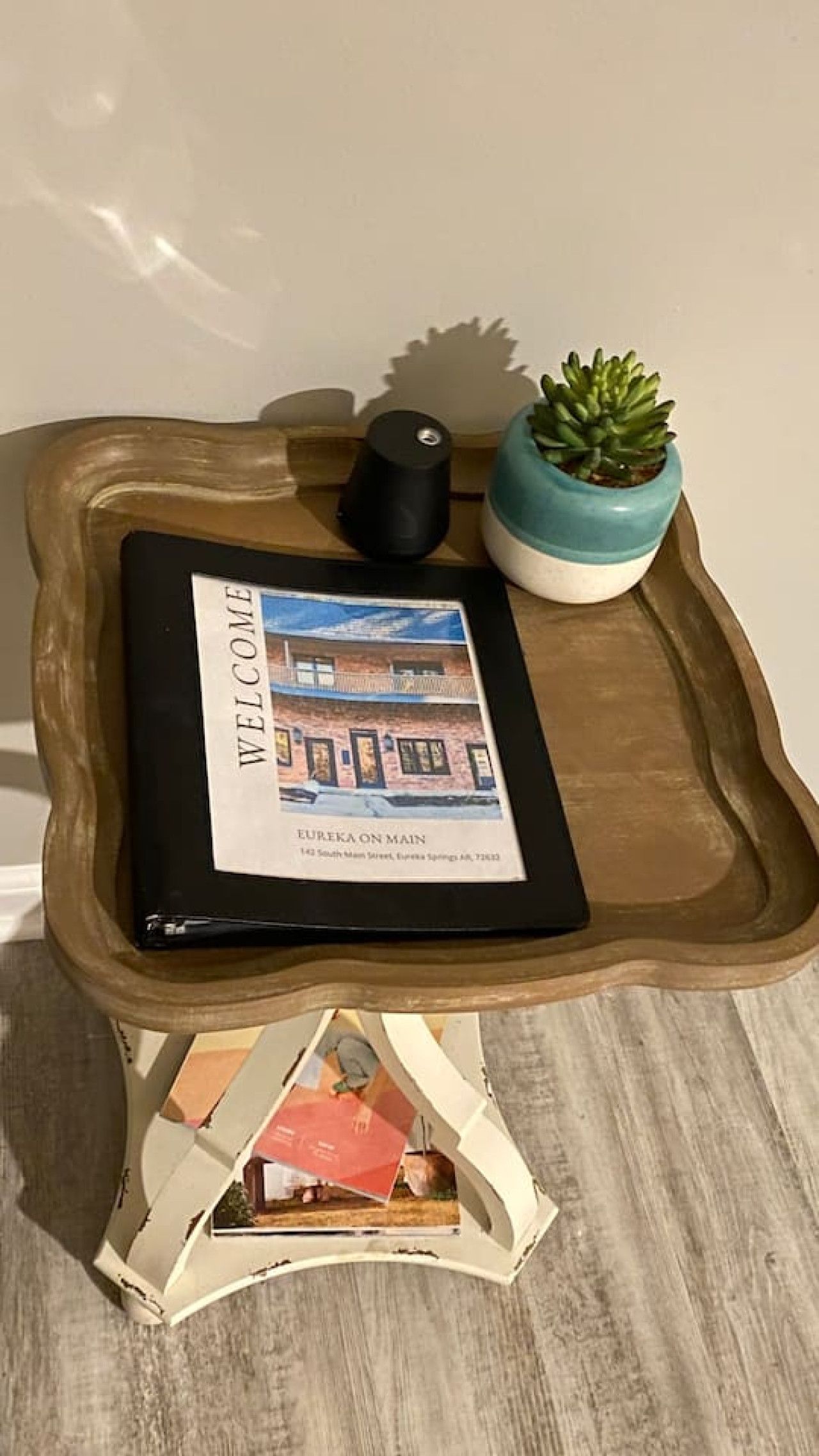 Small white side table with a tray, black cup, succulent, and magazines on a tiled floor.