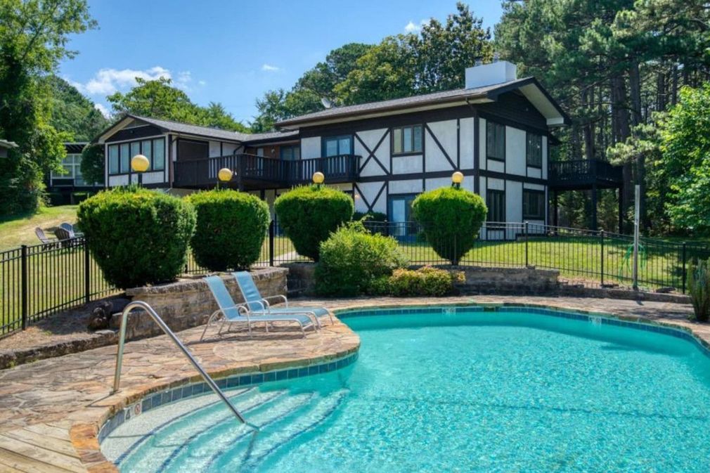 Backyard pool with turquoise water, stone deck, lounge chairs, and a Tudor-style house behind trimmed hedges