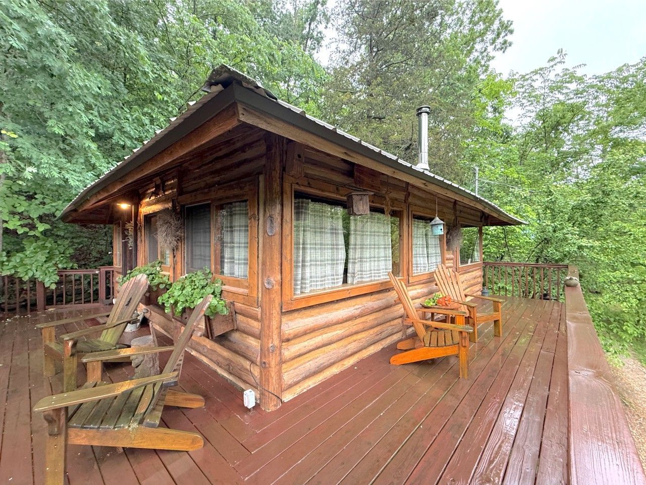 Wooden cabin on a rain-soaked deck with patio furniture, surrounded by dense green trees