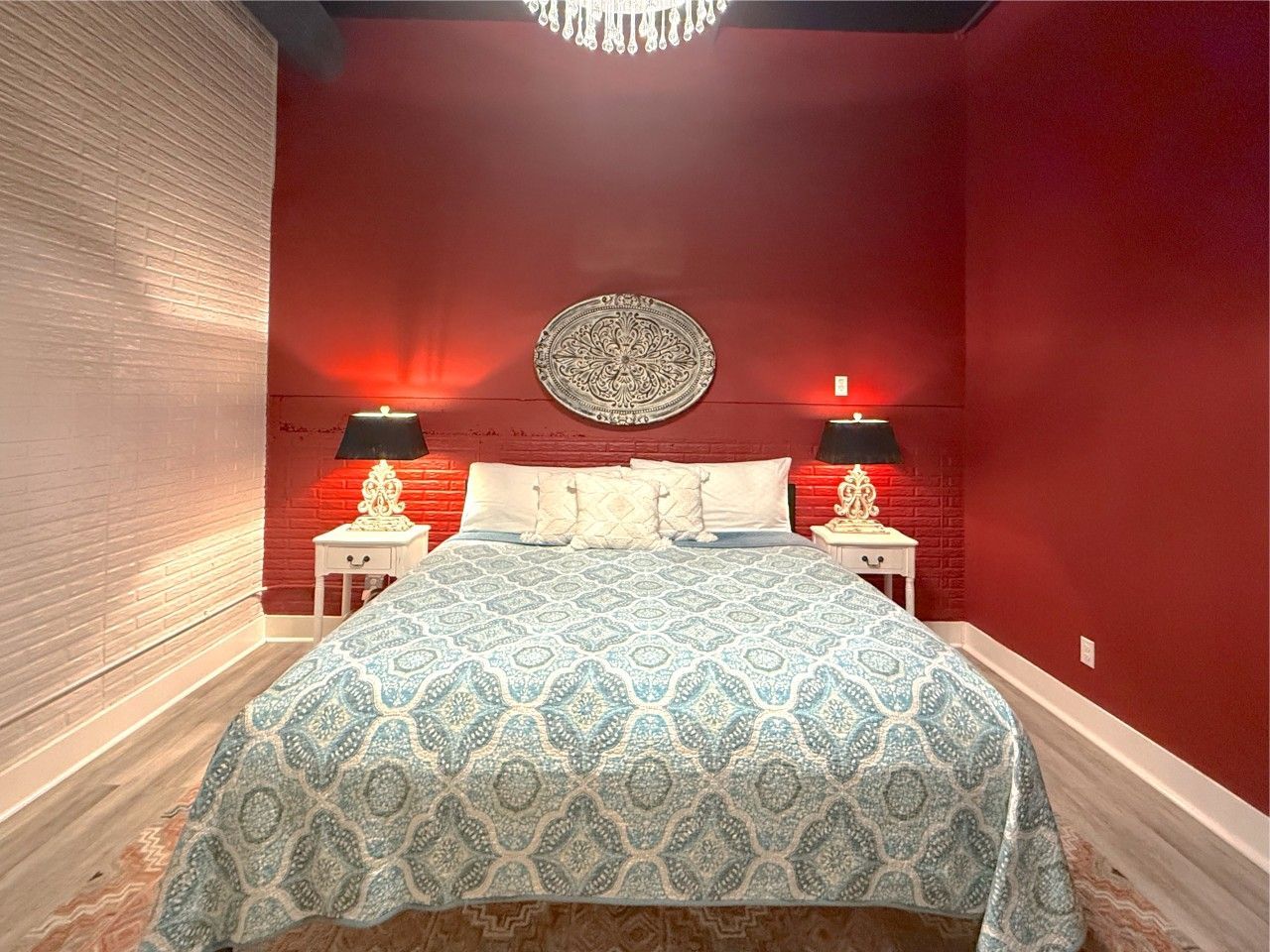 Red bedroom with a large bed, patterned bedding, matching nightstands, and wall art above the headboard
