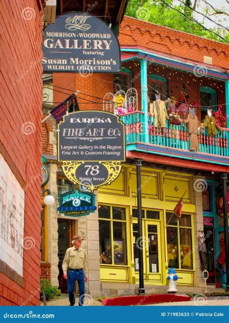 Colorful gallery storefront with hanging sign, balcony, and a person standing by the entrance