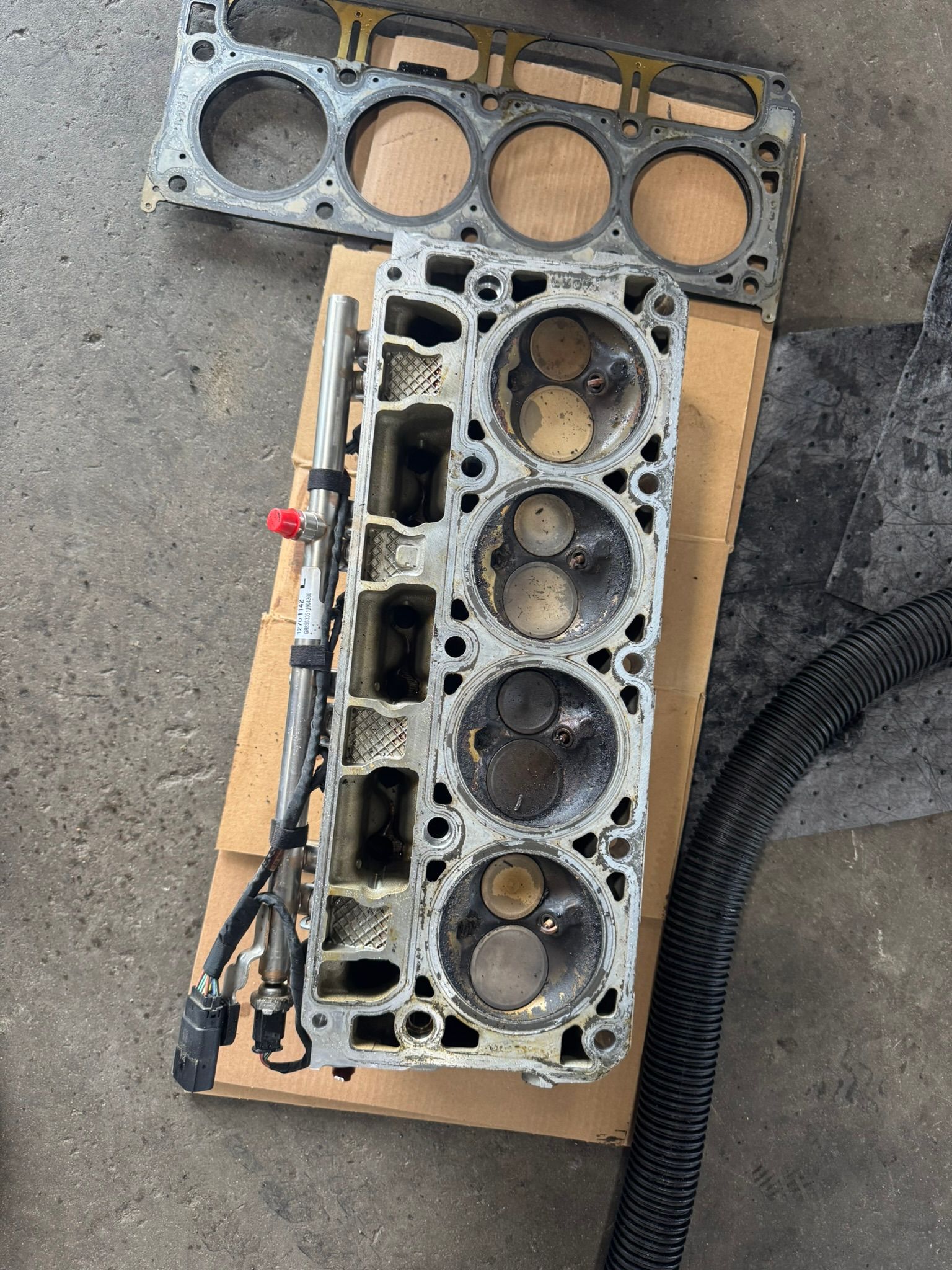 Engine cylinder head with valves and gasket on a cardboard box.