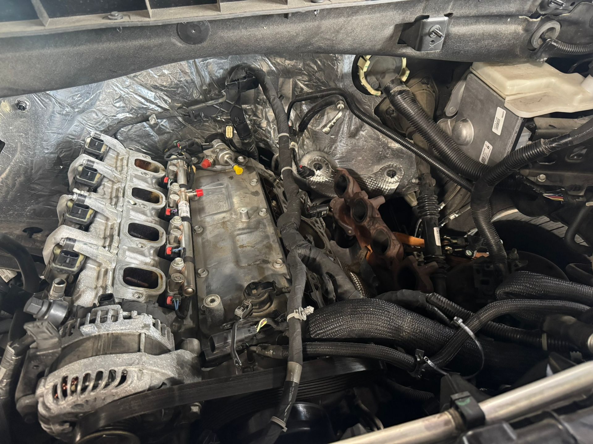 Engine bay with removed parts, showing engine block, manifolds, and wiring harnesses.