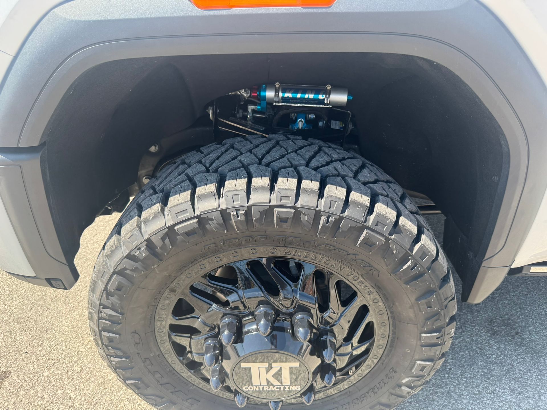 Black lifted truck wheel and tire with blue suspension in wheel well.