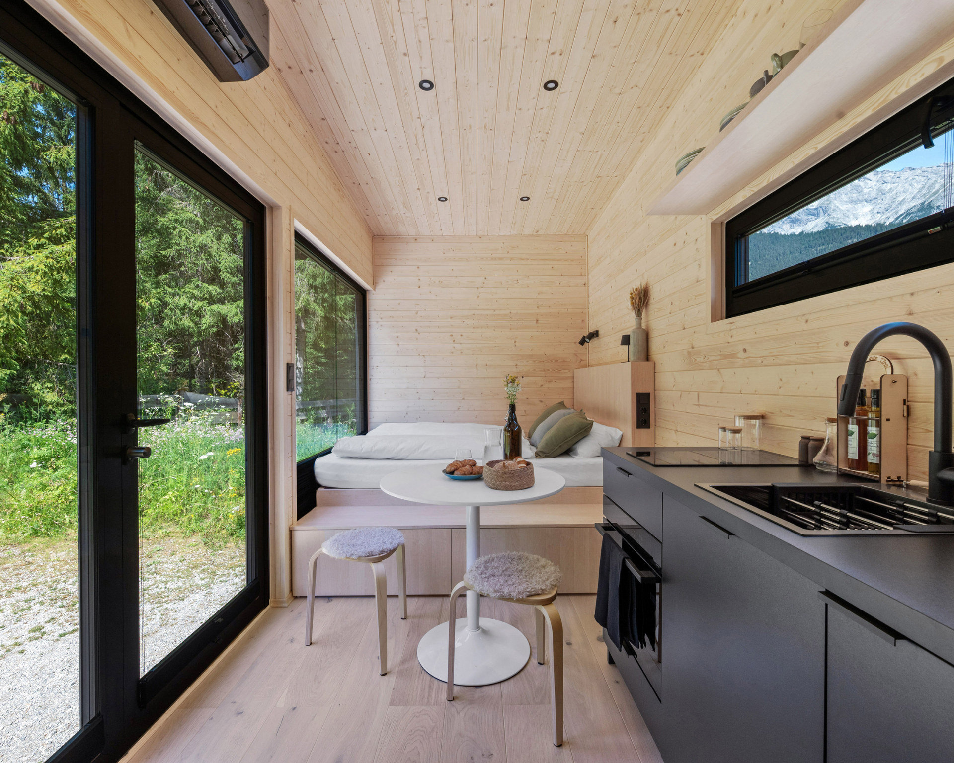 Modern tiny kitchen and dining nook with large windows, light wood walls, and gray cabinets