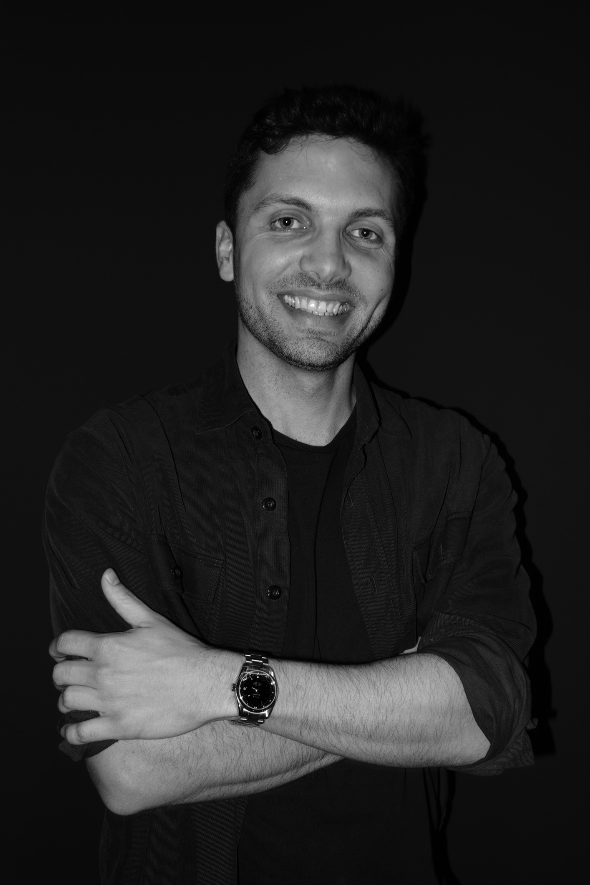 Smiling person in a dark shirt with arms crossed against a black background
