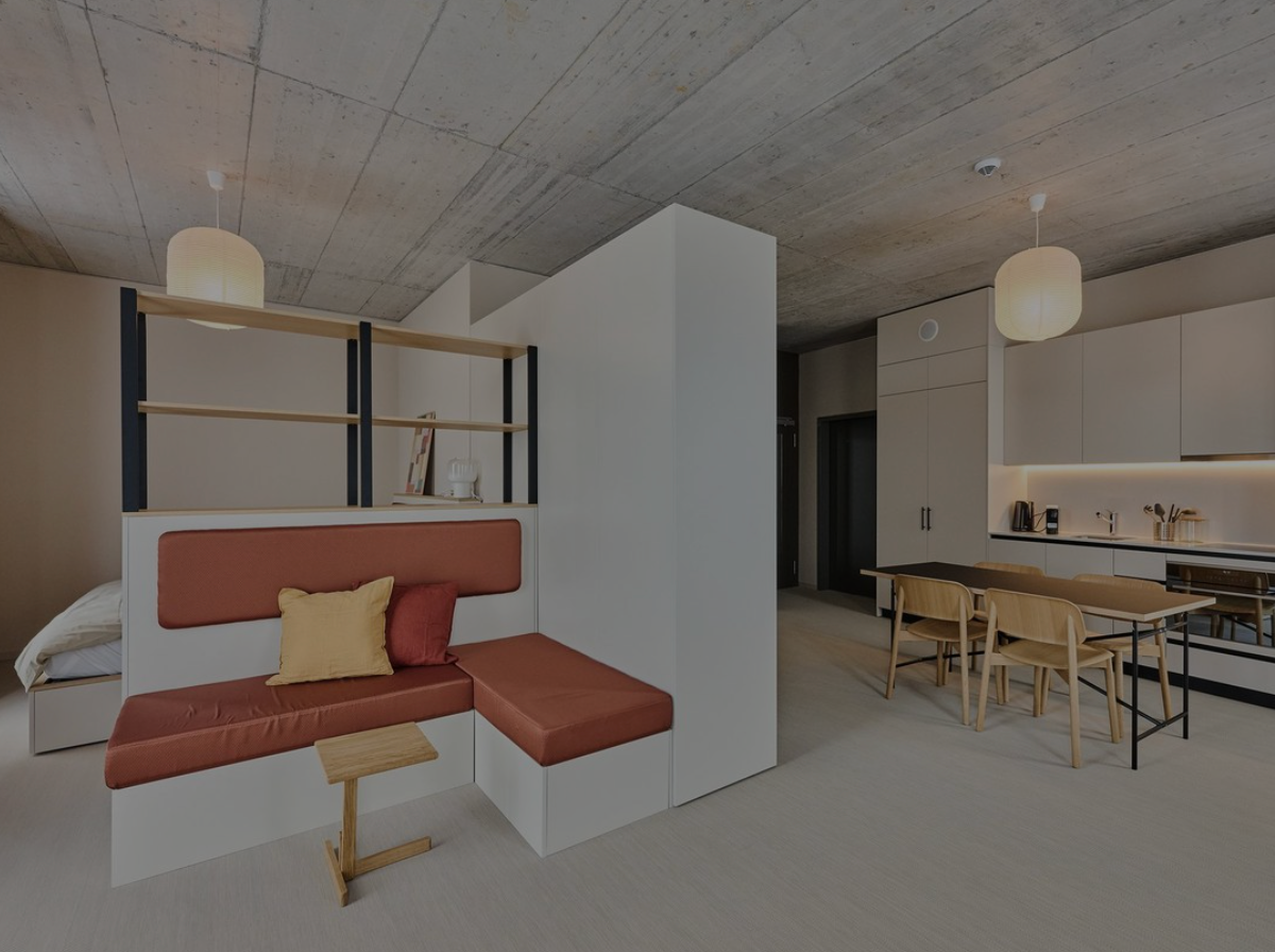Modern minimalist apartment interior with a bed nook, red bench seating, and a kitchen-dining area