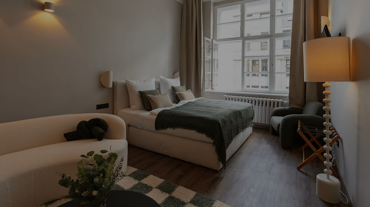 Cozy bedroom with a bed by a large window, floor lamp, chair, and couch in soft neutral tones