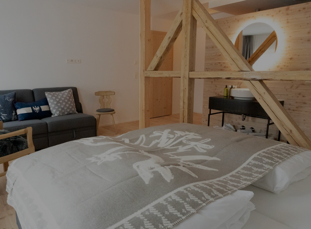 Bedroom with a bed in front, wooden loft frame, sofa, and desk in a bright room