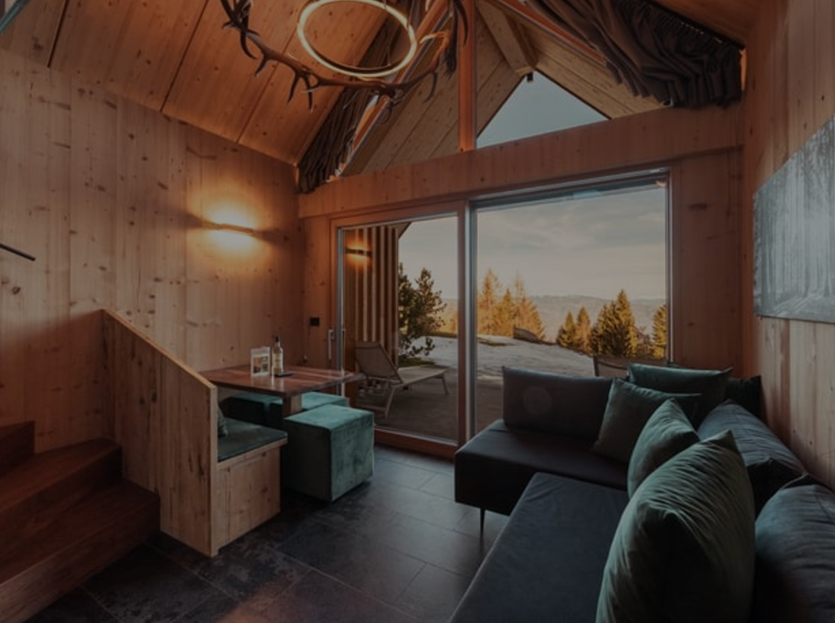Cozy wooden cabin interior with sofa, desk, and large window overlooking a snowy mountain view
