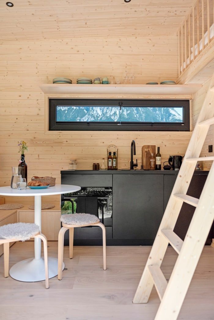 Bright wooden loft interior with a small kitchen, dining table, and ladder to a loft bed.