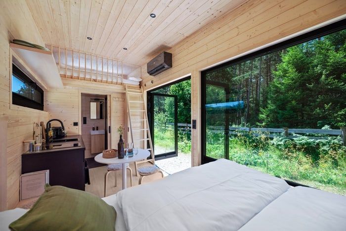Modern bedroom cabin with large windows, wood ceiling, and forest view outside